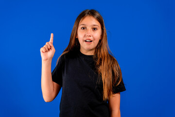 Pretty hispanic preteen girl raising her index finger while smiling, voluntarily lending herself to take action. Positive attitude. Will concept