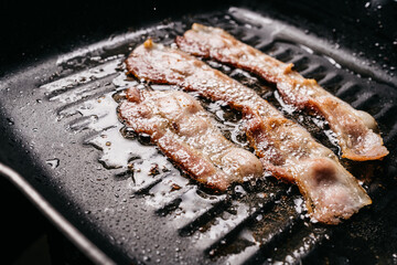 Close up of frying sizzling bacon strips in a pan with hot greasing bacon oil for making crispy bacon. with copy space. Keto snack meal.