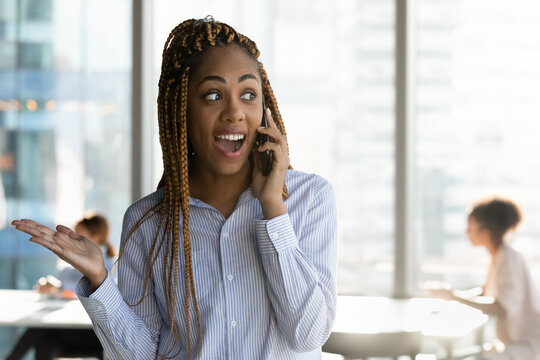 Emotional happy young african american business woman hearing amazing news in phone call conversation, feeling excited of getting profitable job offer or startup opportunity in modern office room.
