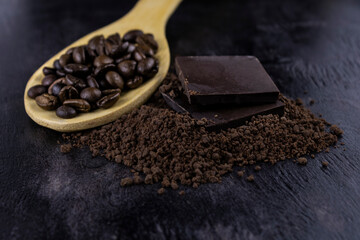 a crumb of dark chocolate and two whole bars with coffee beans on a wooden spoon
