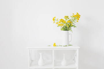 yellow wild summer flowers in jug on white vintage interior