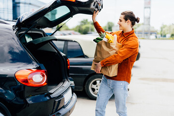 man putting bags with product in car trunk copy space - obrazy, fototapety, plakaty