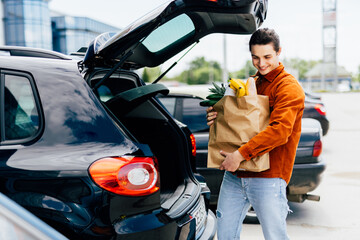 man putting bags with product in car trunk copy space
