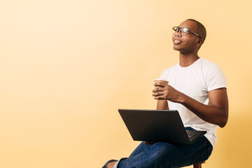 Young black African American man holds a laptop and a cup of coffee.