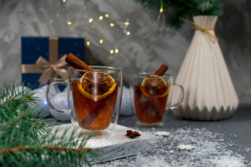 Christmas card. Two glass cups of tea with lemon and cinnamon sticks close-up on a Christmas background. Warm medicinal winter tea in glass cups on the background of a pine branch.