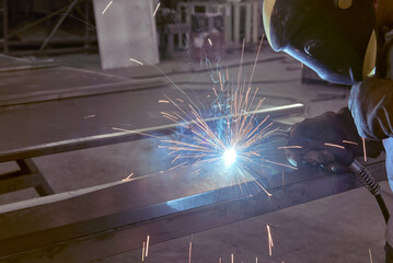 man processes metal with gas electric welding.