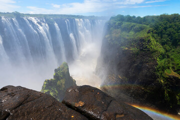 Victoria Falls National Park from over the rocks near the cliff in Zimbabwe side. Tourist destination for nature lovers. Huge water flow, misty air and rainbow visible