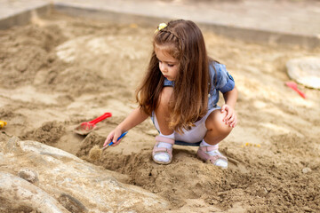 Cute little girl digging sand to find bones in the sandbox.