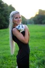 Fototapeta premium beautiful young woman with her bunny. Blonde lady smiling and holding cute rabbit. Summer outdoor park location. People and pets concept.