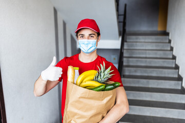Deliver man worker in red color uniform handling bag of food, fruit, vegetable give costumer in front of the house. Postman give thumb up gaurantee good service. Express grocery delivery concept