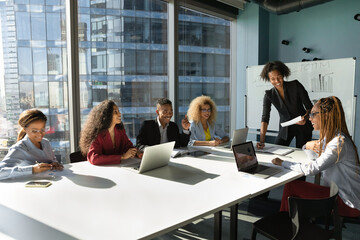 Smiling pleasant young african american business woman leader mentor holding negotiations or brainstorming meeting with motivated biracial teammates, sharing knowledge or discussing project.