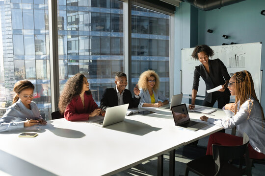 Smiling pleasant young african american business woman leader mentor holding negotiations or brainstorming meeting with motivated biracial teammates, sharing knowledge or discussing project.