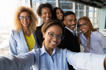 Smiling beautiful millennial african american business woman making selfie photo with motivated happy mixed race diverse colleagues partners, having fun entertaining together in modern workplace.