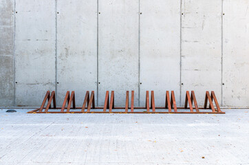 Row modern, empty bicycle racks, made of rusted metal or corten steel. Concrete wall in the background.
