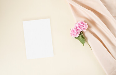 Mockup blank wedding invitation card with nude fabric, pink hydrangea flowers on the beige background

