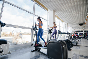 Two young beautiful girls exercise in the gym wearing masks during the pandemic. Social distancing in public places.