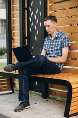 A young man at a photo shoot with a laptop, and in a plaid shirt with short sleeves.