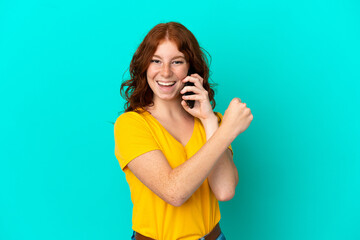 Teenager reddish woman using mobile phone isolated on blue background celebrating a victory
