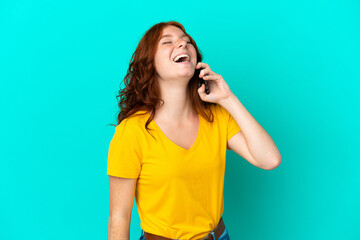 Teenager reddish woman using mobile phone isolated on blue background laughing