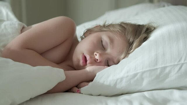 Peaceful little girl sleeping on bed in room. Bedtime rest. Carefree childhood. Sunny morning. Sleeping baby concept. 4K, UHD