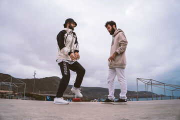 Two Caucasian guys, dressed in casual outfits, dance shuffle in the middle of the street