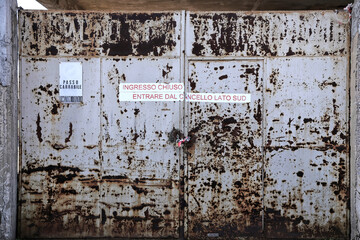 Old industrial iron gate. Abandoned rusty industrial door with faded lettering in Italian "entrance closed"
