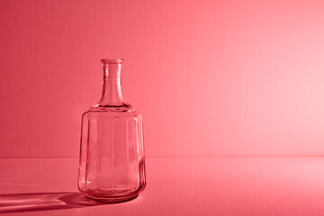 Glass empty open bottle with copy space. Graphic still life with light and shadow in red light. The concept of glass containers, recyclable materials or alcoholism. Large creative vase. Open flask