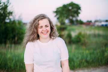 Fototapeta premium Portrait Of Beautiful Plus Size Young Woman In White Shirt Posing In Summer Field Meadow At Sunset Background