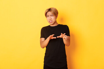 Portrait of disgusted picky asian guy, refusing and grimacing, standing yellow background - obrazy, fototapety, plakaty