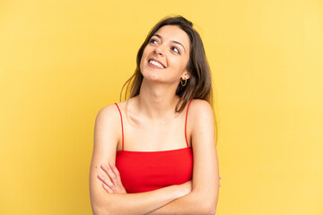 Young caucasian woman isolated on yellow background looking up while smiling