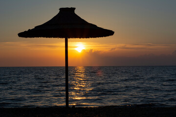 Beach umbrella and the setting sun by the sea on a deserted beach concept for completing a summer...