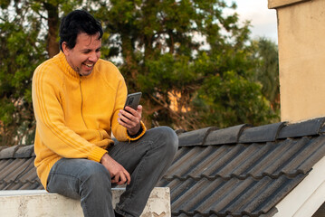 Auto retrato de hombre blanco en el tejado en un dia de otoño con campera amarillo y un celular...
