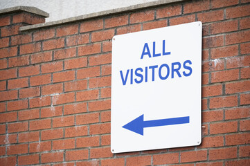 All visitors arrow direction sign on wall of car park