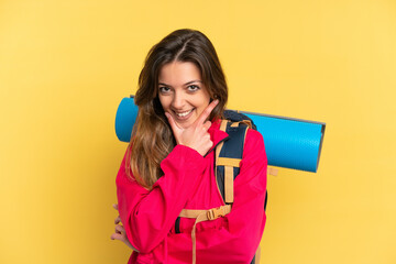 Young mountaineer man with a big backpack isolated on yellow background happy and smiling