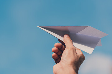 Man's hand holding paper plane, Blue sky background with natural light., Flying to the freedom concept.