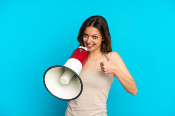 Young caucasian woman isolated on blue background holding a megaphone with thumb up
