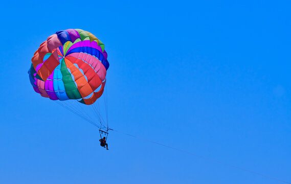 Man flying on rainbow-colored parachute in blue sky.