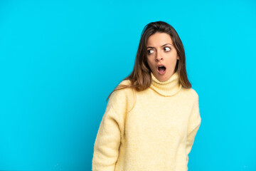 Fototapeta premium Young caucasian woman isolated on blue background doing surprise gesture while looking to the side