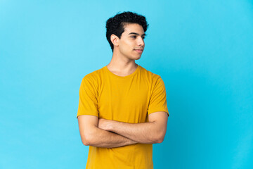 Young Venezuelan man isolated on blue background looking to the side