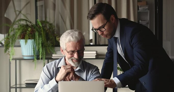 Multi Generational Men Workmates Using Laptop Discuss On-line Project Gathered At Workplace In Office. Mentoring, Younger Helps To Older With Modern Tech Software, Collaborative Task, Teamwork Concept