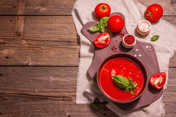 Tomato soup with basil in a bowl. Ripe vegetables, fresh greens, fragrant spices. Vintage wooden table, top view