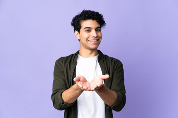 Young Venezuelan man isolated on purple background holding copyspace imaginary on the palm to...