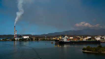 Obraz premium Plant with pipes generating smoke and oil tankers in the port Santiago de Cuba