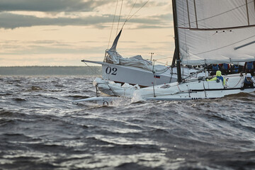 Competition of two sailboats on the horizon in sea at sunset, the amazing storm sky of different colors, race, big waves, sail regatta, cloudy weather, only main sail, sun beams