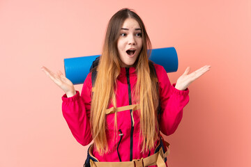 Young mountaineer girl with a big backpack isolated on pink background with surprise facial expression