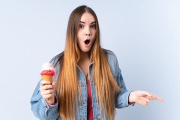 Young woman with a cornet ice cream isolated on blue background surprised and pointing side