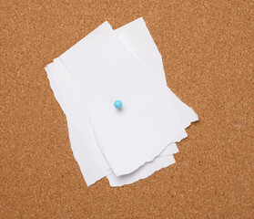 torn white blank white sheet of paper affixed with a plastic button on a brown cork board