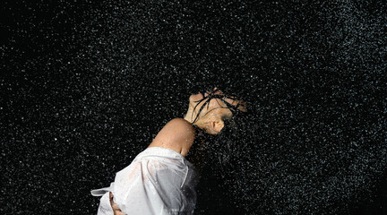 beautiful woman of Caucasian appearance with black hair dances in drops of water on a black background