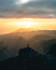 Fototapeta na wymiar Man stands alone on the peak of rock during sunrise at Pico do Arieiro in Madeira. High quality photo