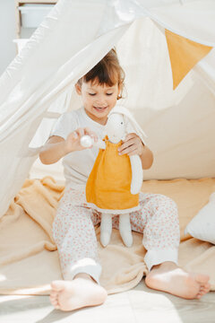 Six years cute girl playing in teepee with fabric tilda bunny at home